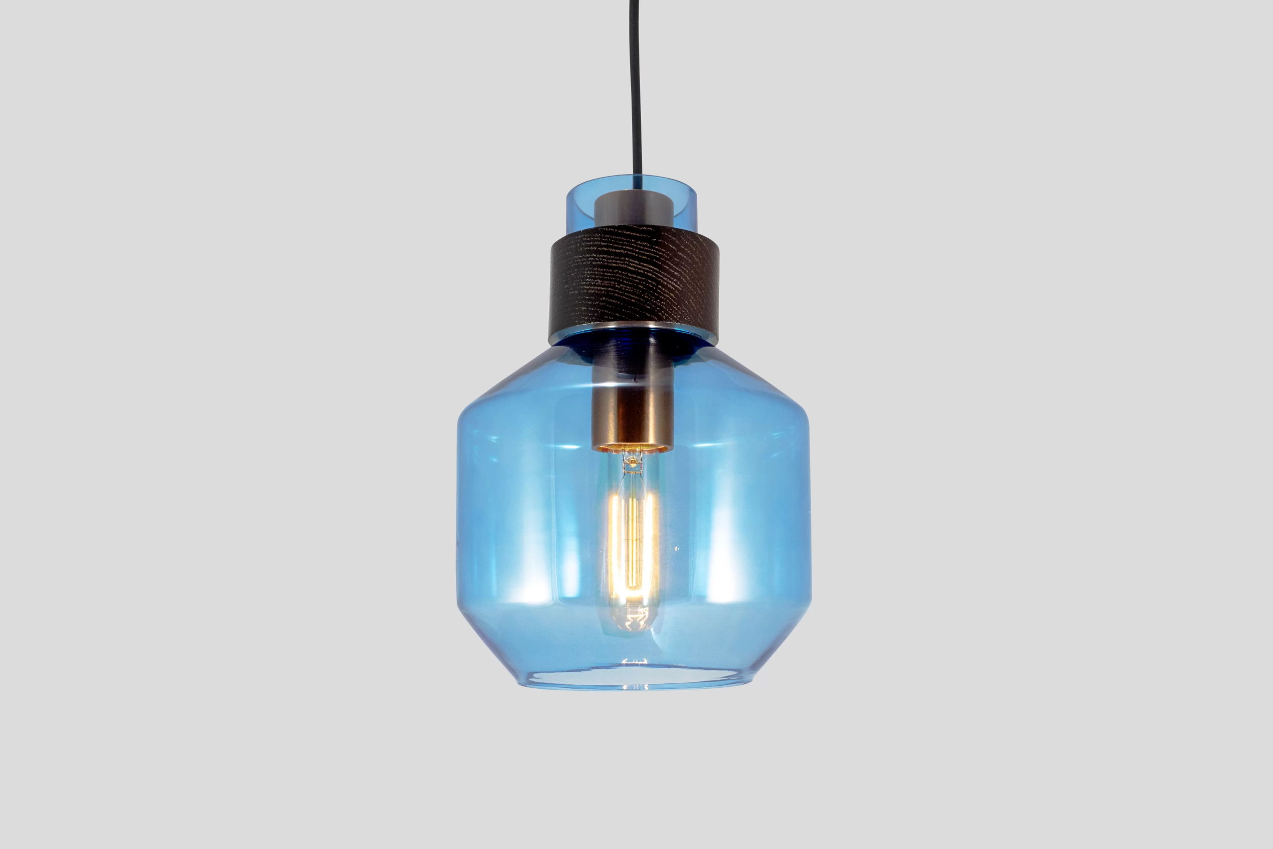 El colgante Montri es una lámpara fabricada en cristal y madera, de estilo industrial. Viene disponible en color naranja, gris fume y ámbar.