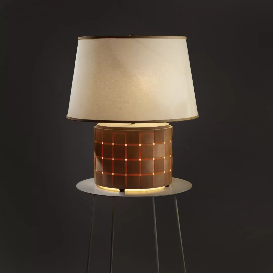 Lámpara de mesa Brilla. Lámpara confeccionada artesanalmente. Base de trenzado en madera Guatambú con pantalla de tela rígida. La base contiene luz interior